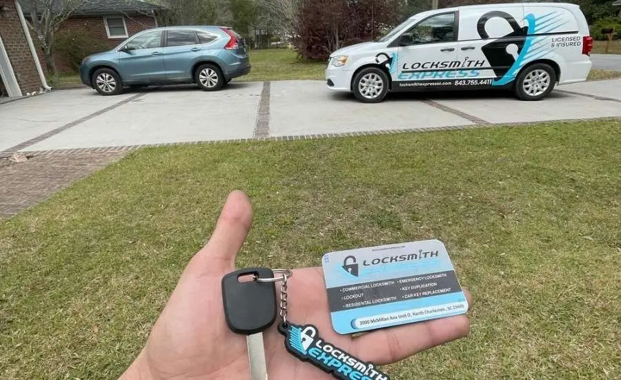 Hand holding a car key locksmith express card and keychain with a locksmith express van in the background.