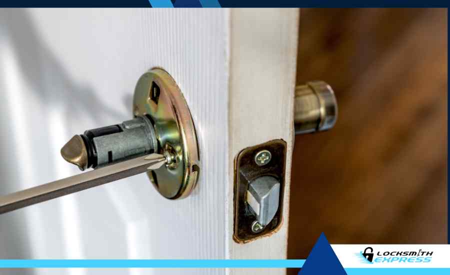 A screwdriver tightening the set screw on the side edge of an open door.