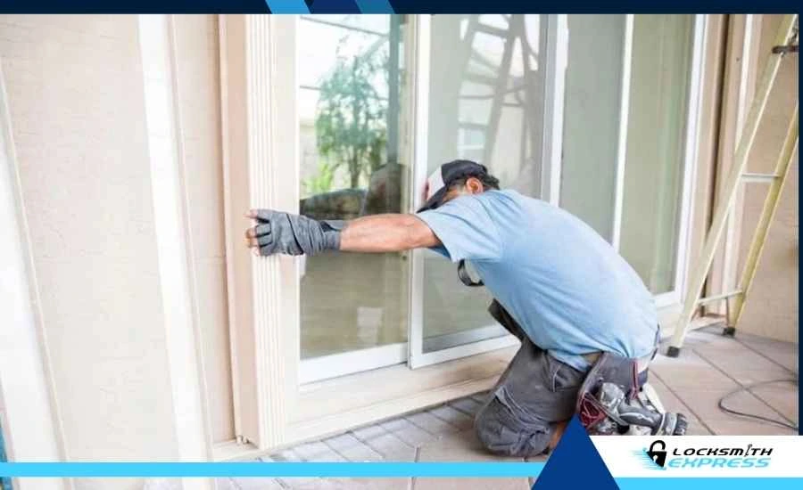 Locksmith kneeling outside a glass storefront door, repairing a lock while wearing gloves and a blue shirt.
